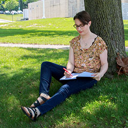 Kristen Wood sitting by a tree and writing