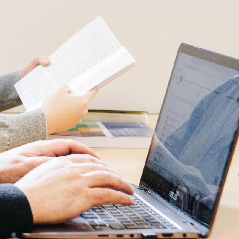 person reading a book while another person types on their laptop