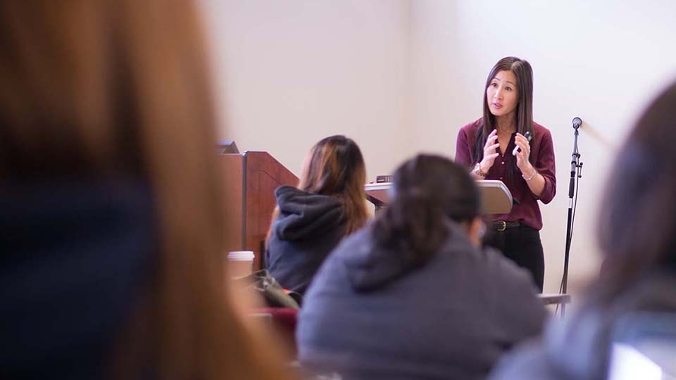 Female teacher speaking in front of students inside a classroom