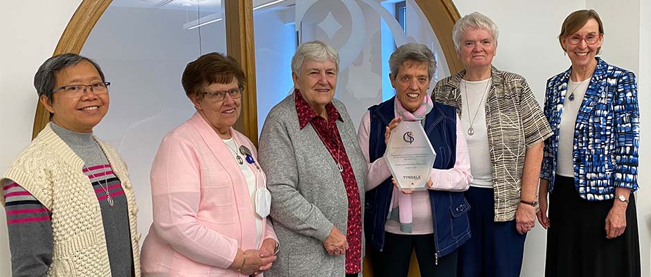 A group of women smiling with an elder holding up an glass trophy