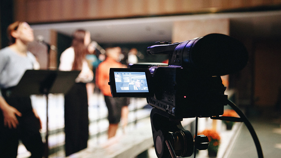 A camera recording singers at the front of the chapel