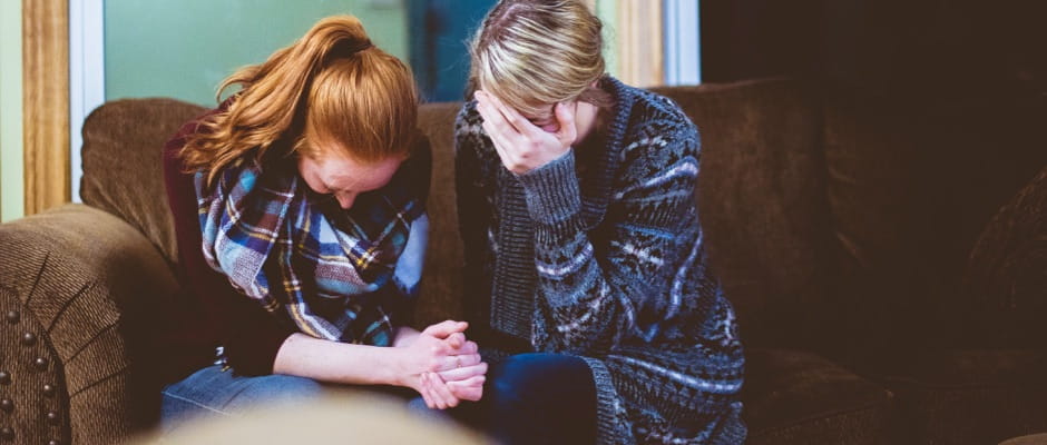 Two females praying together on a couch