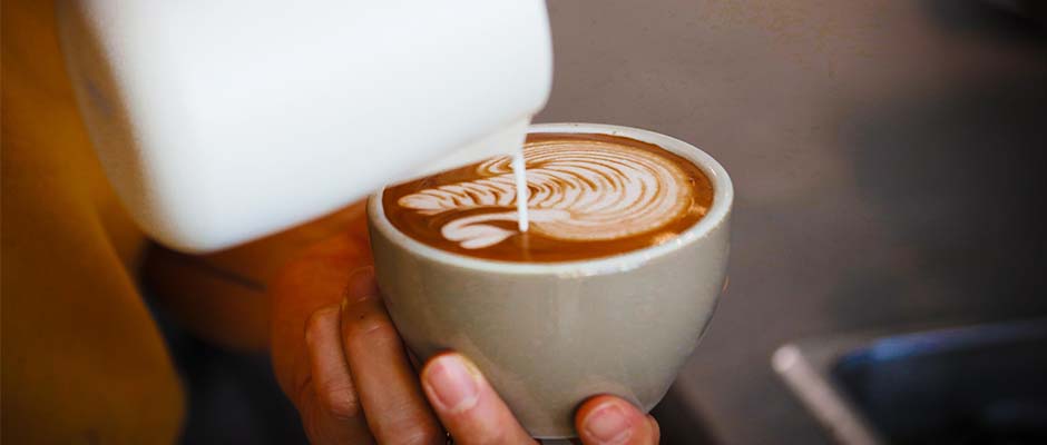 A cup of milk poured into a cup of coffee held by a hand