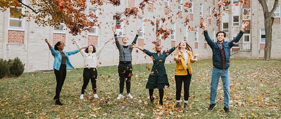 Tyndale Students smiling with joy and open arms as leaves fall to the ground