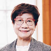 Short haired woman with red eyeglasses smiling in a grey blazer