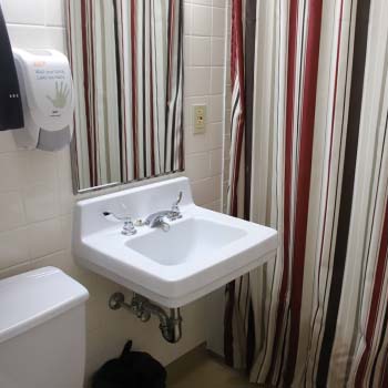 A washroom with a single sink, toilet and soap dispenser against a stripped patterned shower curtain