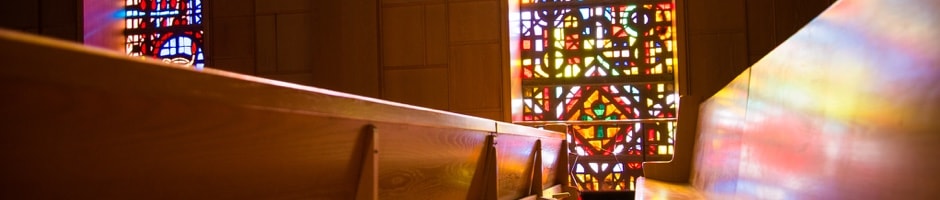 Stained glass windows reflecting light on some church pews in the Tyndale Chapel