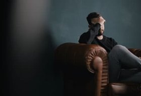 a man holds his head while sitting on sofa