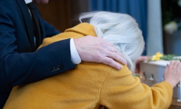 older woman leaning over a coffin distraught