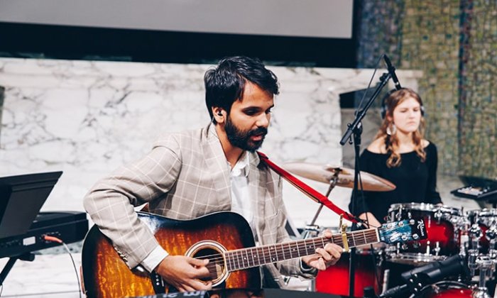 Man playing guitar with woman on drums in the background