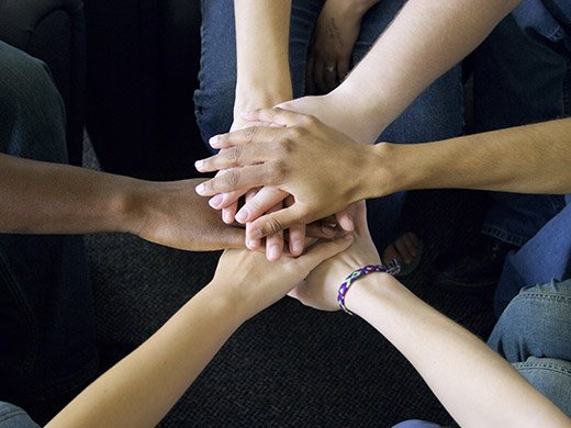 A view from above of a circle of six people's hands piled on top of one another