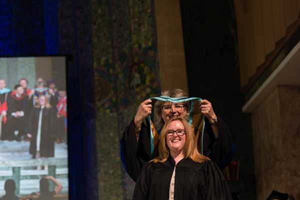 Faculty member bestowing convocation hood over graduate