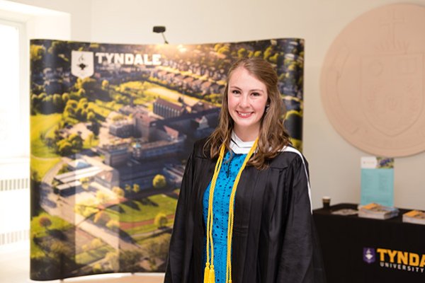 A graduate in front of a Tyndale poster/sign