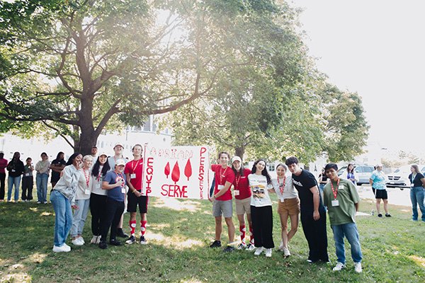 Students representing the Adrian House holding the crest flag that says Perseverance, Equip, Serve.