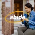 A woman on her phone and the word abide