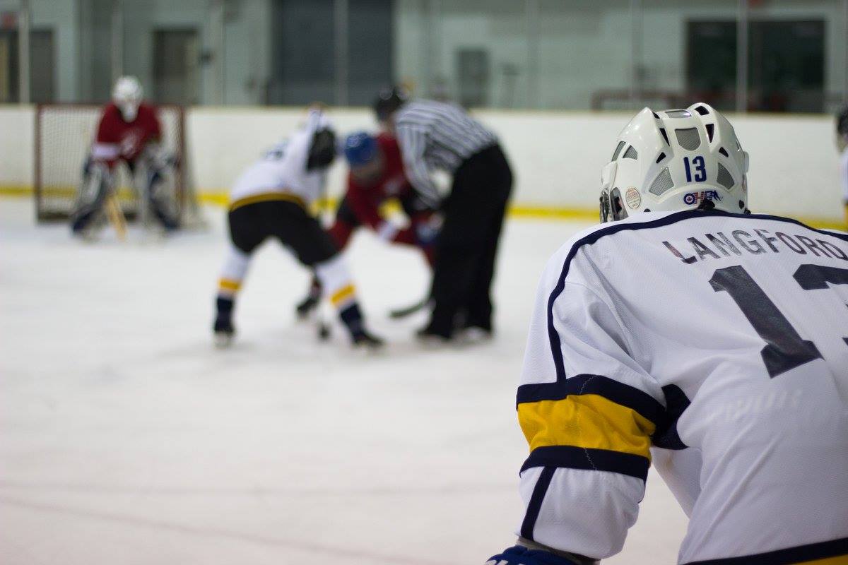 Hockey player in foreground looking at faceoff between 2 players beside a referee